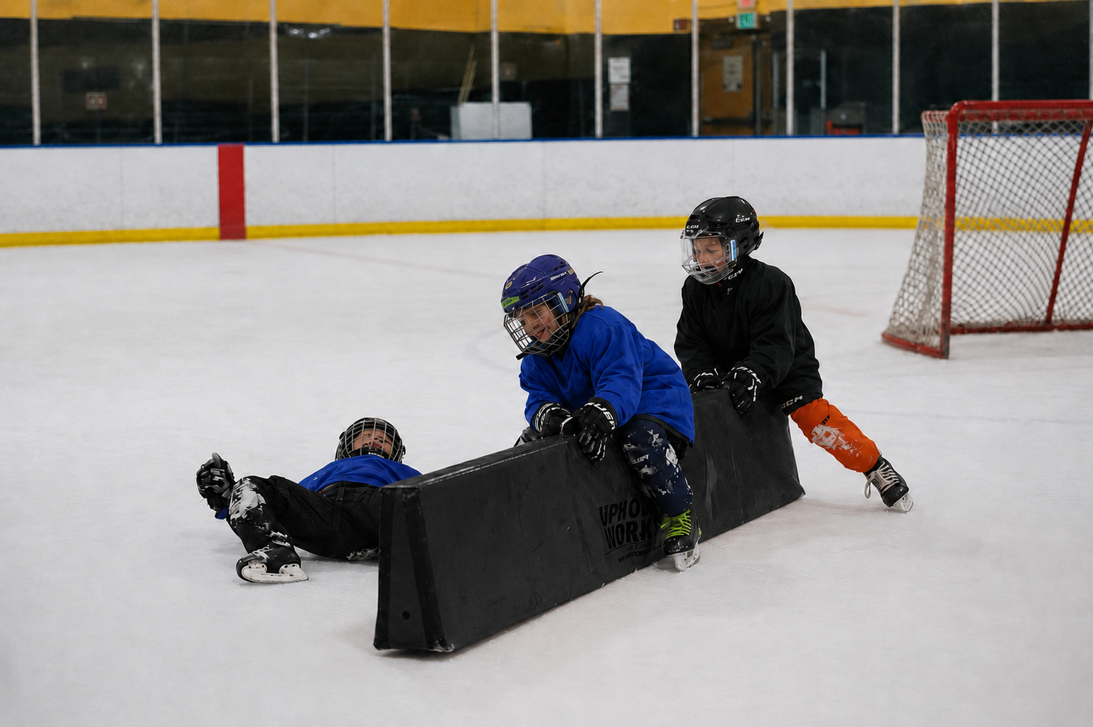 Young ice hockey players training with an orange development barrier at the rink.