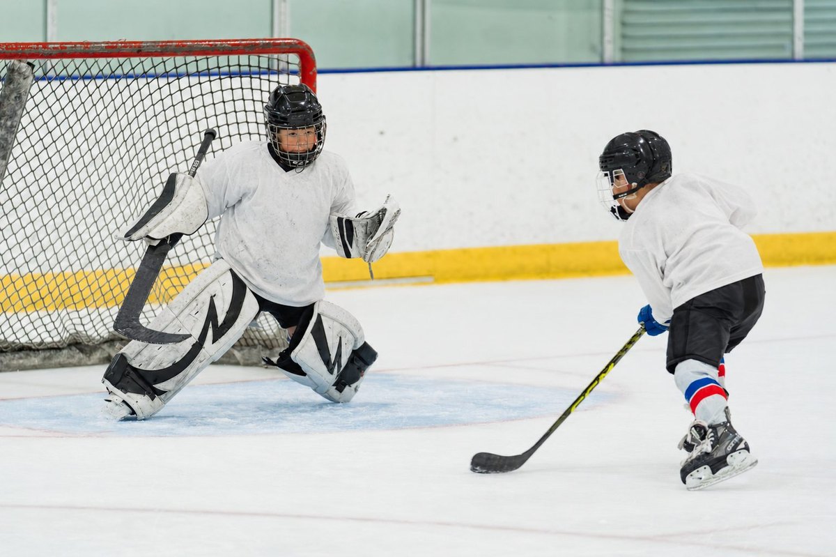 Youth hockey action at the rink with a goaltender and player near the net.