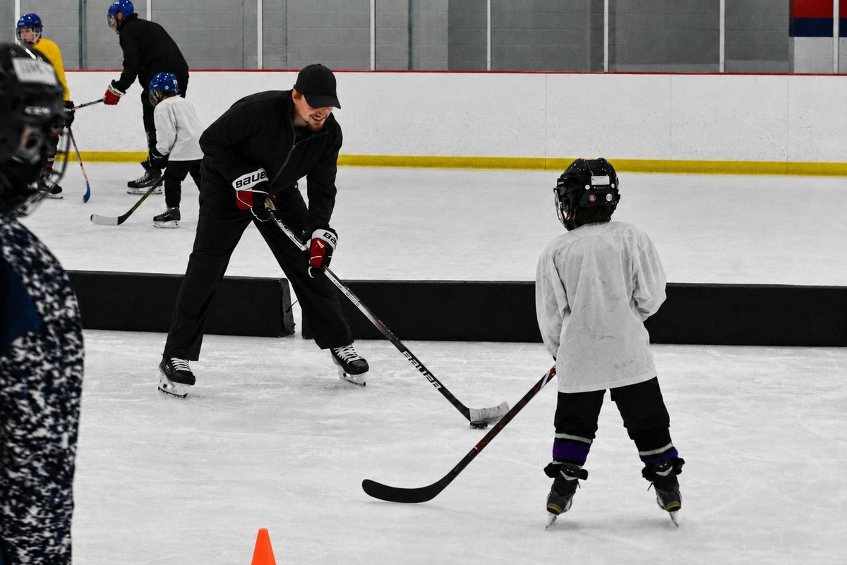 Silverbacks coach helping a young beginner with their helmet at the rink.