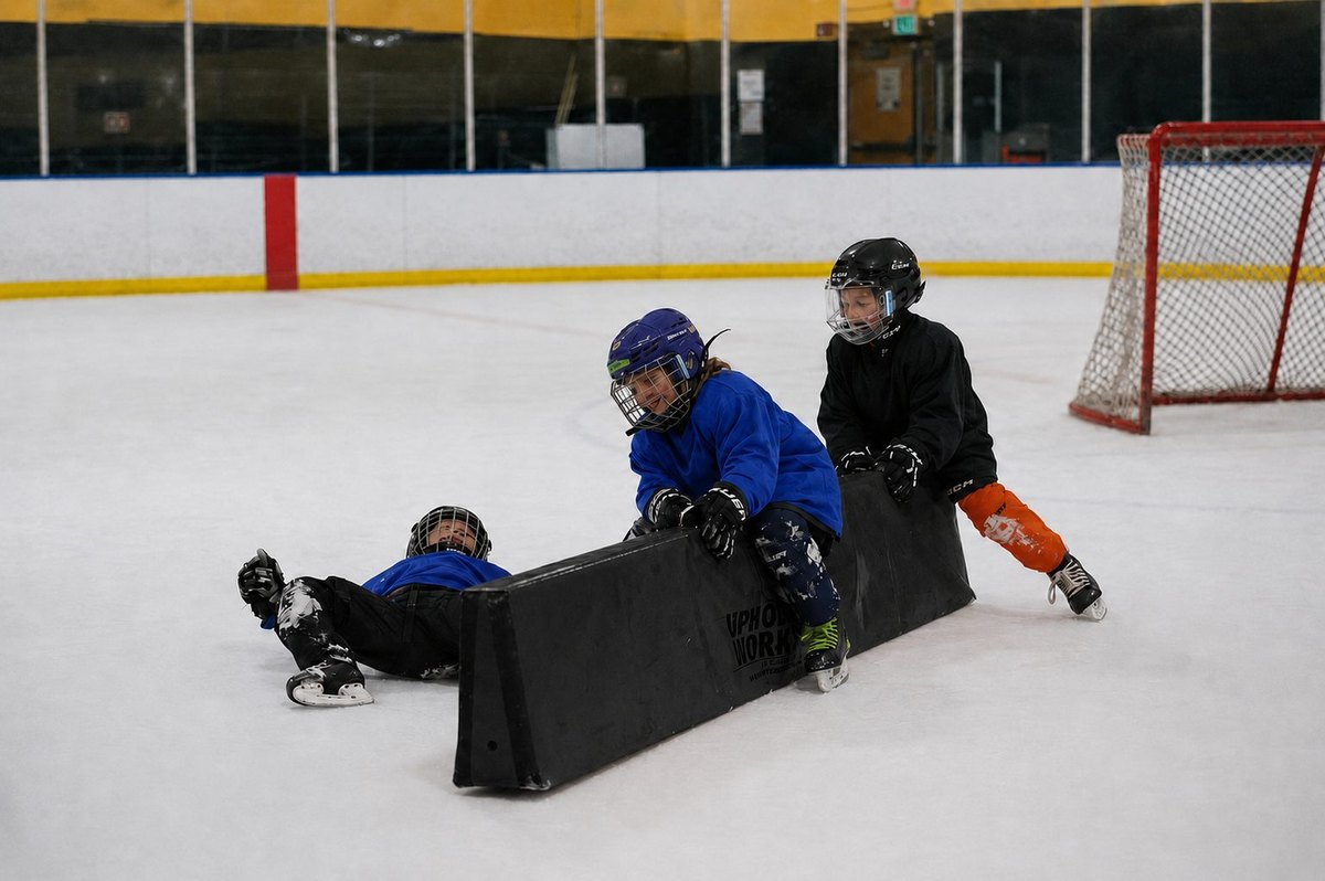 Young ice hockey players training with an orange development barrier at the rink.